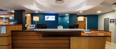 A hotel reception desk with a digital display, a 'Holiday Inn Express' sign, and a 'Reception' sign.
