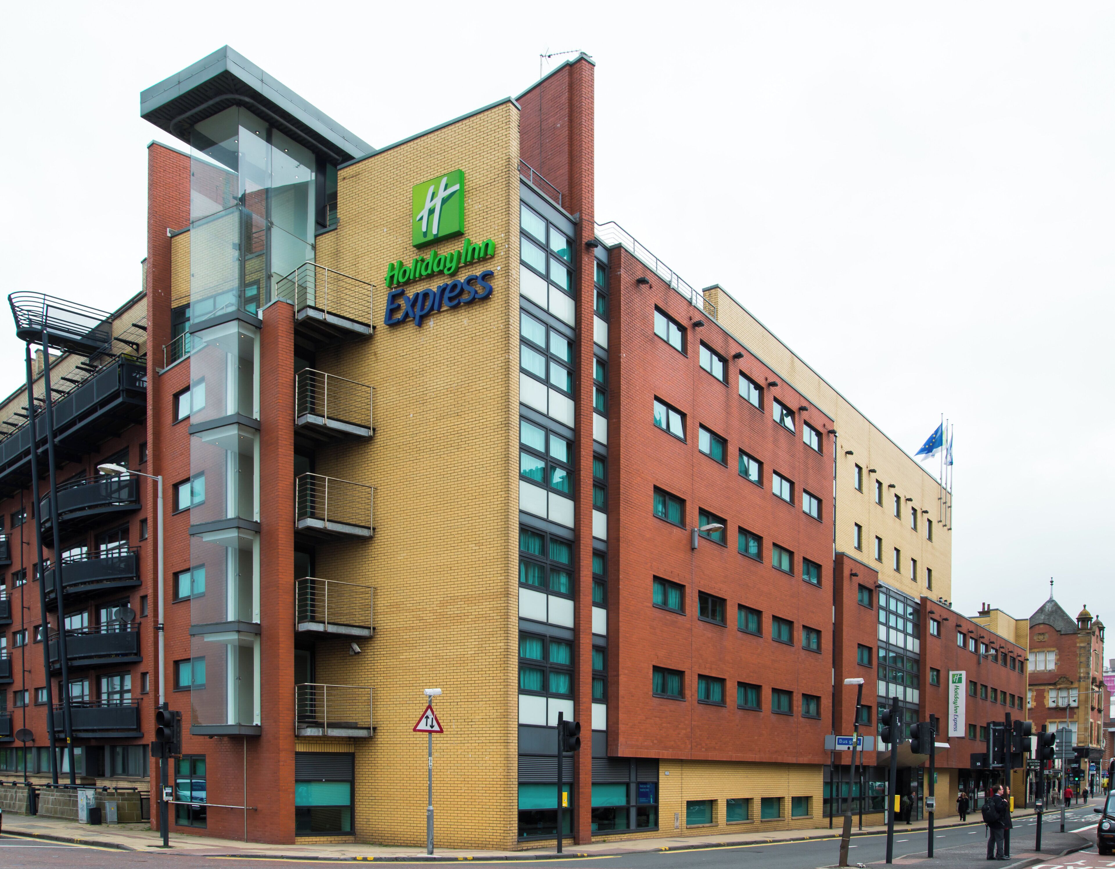 Un edificio de varios pisos con un llamativo letrero de Holiday Inn Express, que presenta un diseño moderno con elementos de ladrillo y vidrio.