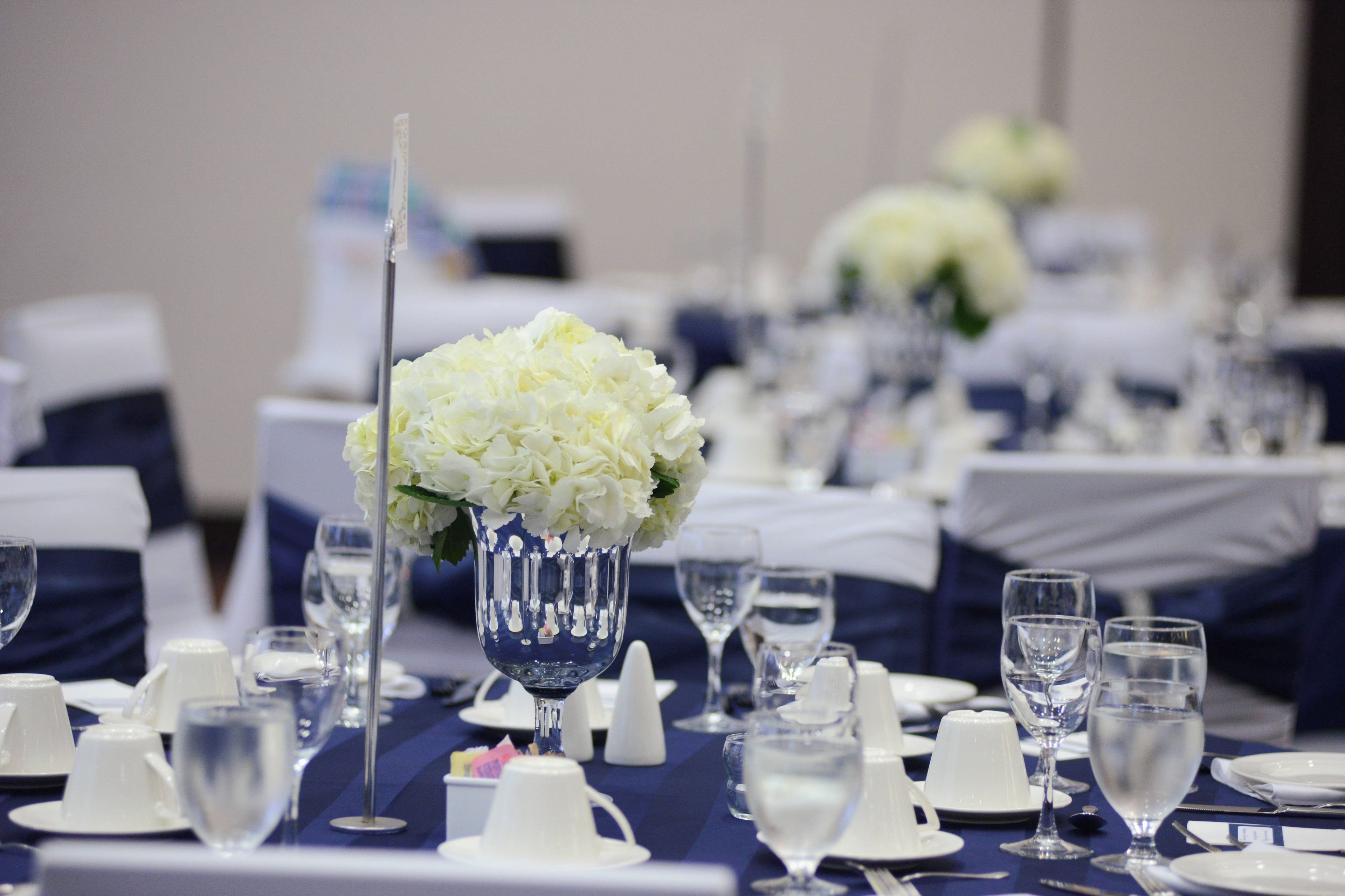 Una mesa de banquete dispuesta con vajilla blanca y un jarrón con flores blancas.