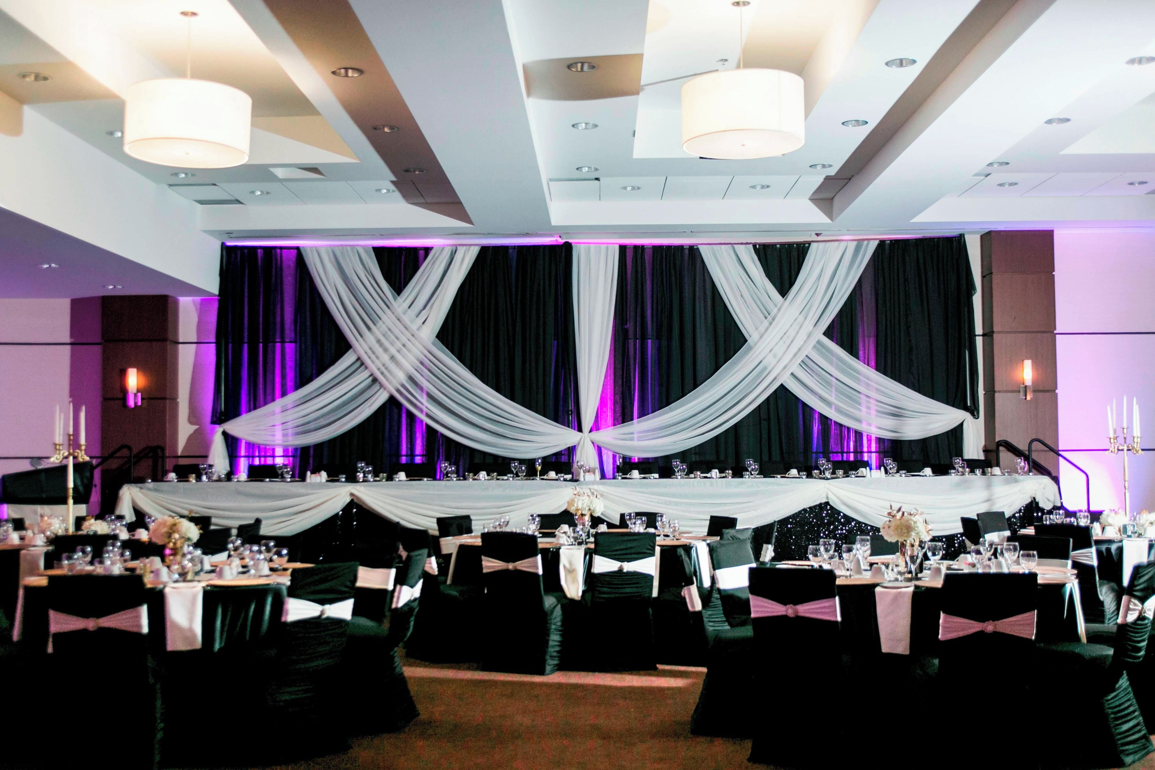 A banquet hall with tables set for a formal event, draped with white fabric, and equipped with chandeliers and candles.