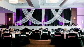 A banquet hall with tables set for a formal event, draped with white fabric, and equipped with chandeliers and candles.