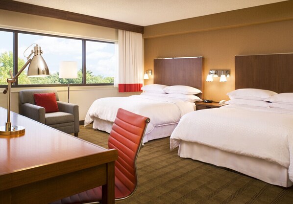 Habitación de hotel con dos camas, un escritorio, una silla, una lámpara y una ventana con cortinas.