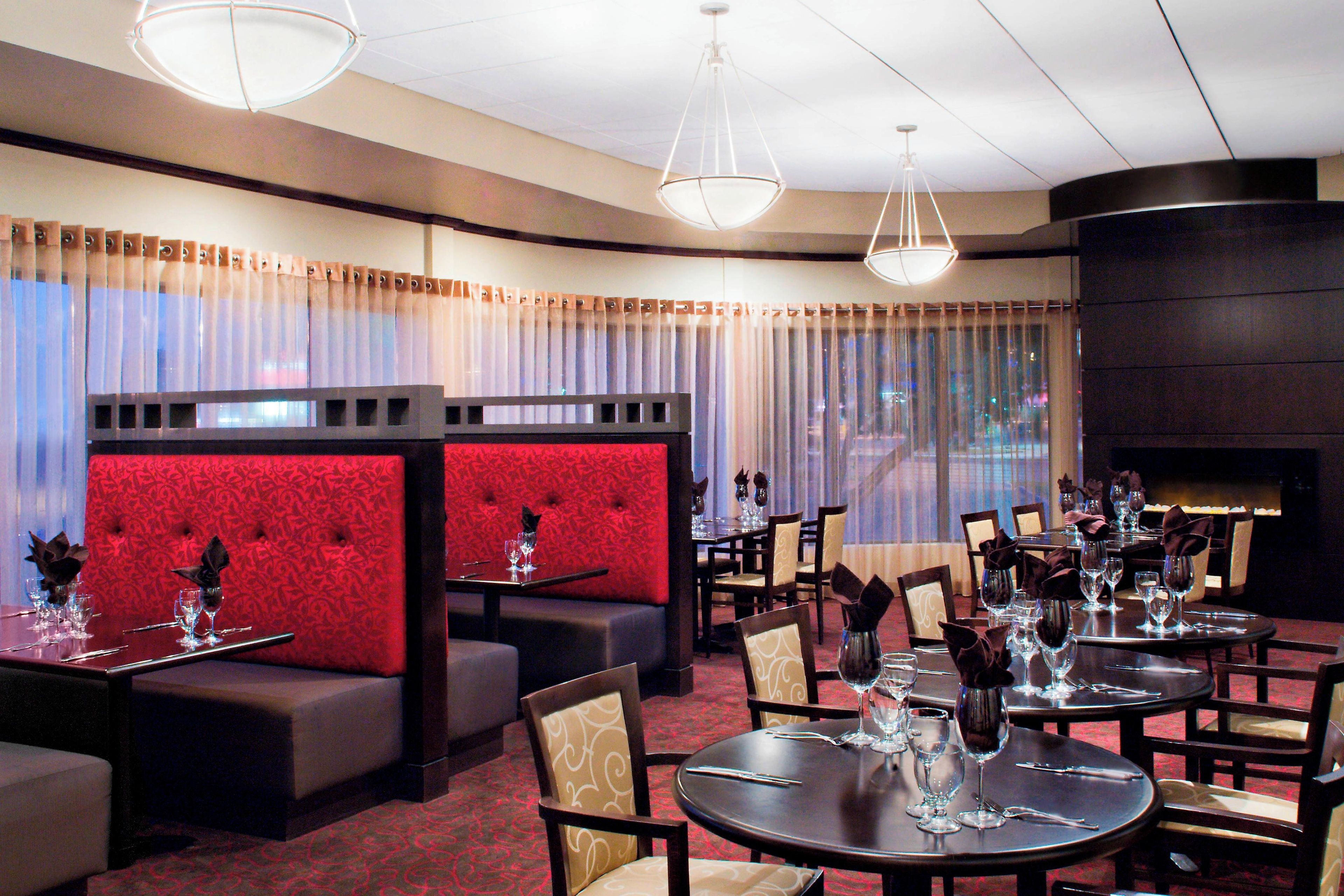 A restaurant with booths, round tables, and a red upholstered wall.
