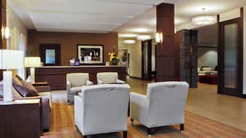 Un vestíbulo de hotel con mostrador de recepción, zona de estar con sillones y una alfombra estampada.