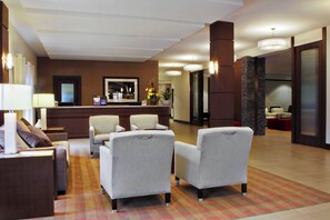 Een hotel lobby met een receptiebalie, een zithoek met fauteuils en een kamerbreed tapijt met een patroon.