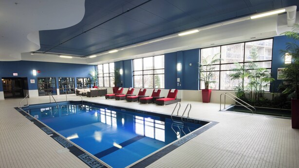 Une piscine intérieure dotée de lignes de démarcation bien visibles, de chaises longues rouges et de grandes fenêtres offrant une vue sur l’extérieur.