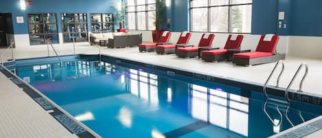 Ein Swimmingpool mit roten Liegestühlen, einer gefliesten Terrasse und großen Fenstern.