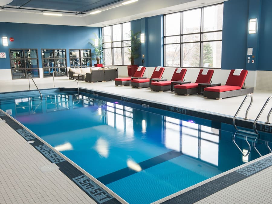 A swimming pool with red lounge chairs, a tiled deck, and large windows.