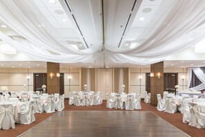 Un amplio y elegantemente decorado salón de banquetes con filas de mesas redondas, cada una con mantel blanco y sillas, y una lámpara de araña central.