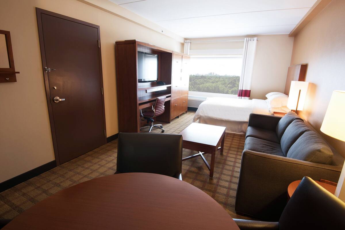 Quarto de hotel com cama, escrivaninha, cadeira, mesa e televisão.