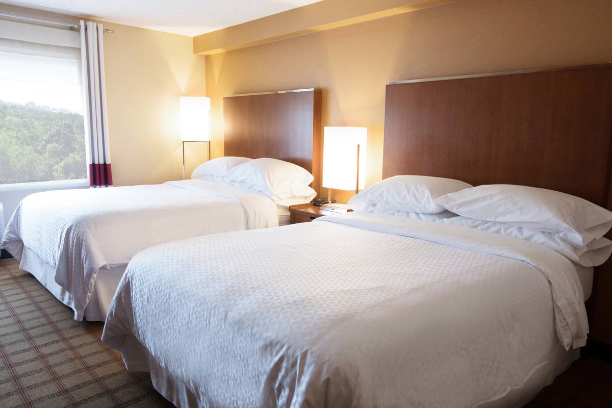 Quarto de hotel com duas camas, uma mesa de cabeceira e uma luminária.