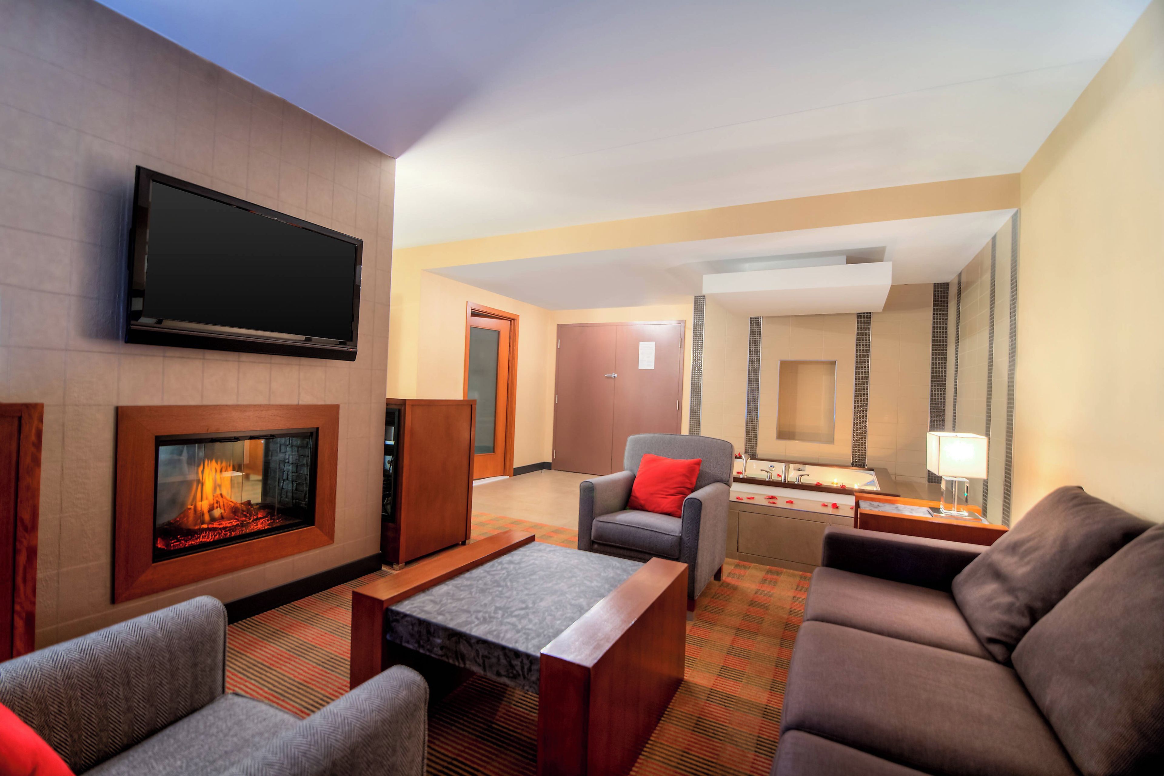 Vestíbulo de hotel con televisor de pantalla plana, chimenea, zona de estar y baño con espejo y lavamanos.