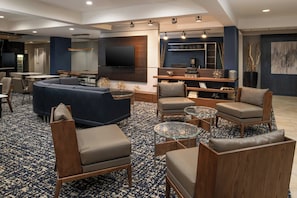 A modern living room with a sectional sofa, armchairs, a glass coffee table, and a flat-screen TV mounted on the wall.