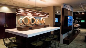 A modern bar area with a white countertop, black wireframe chairs, and a unique wooden light fixture. - Courtyard by Marriott Shreveport Airport (Shreveport)