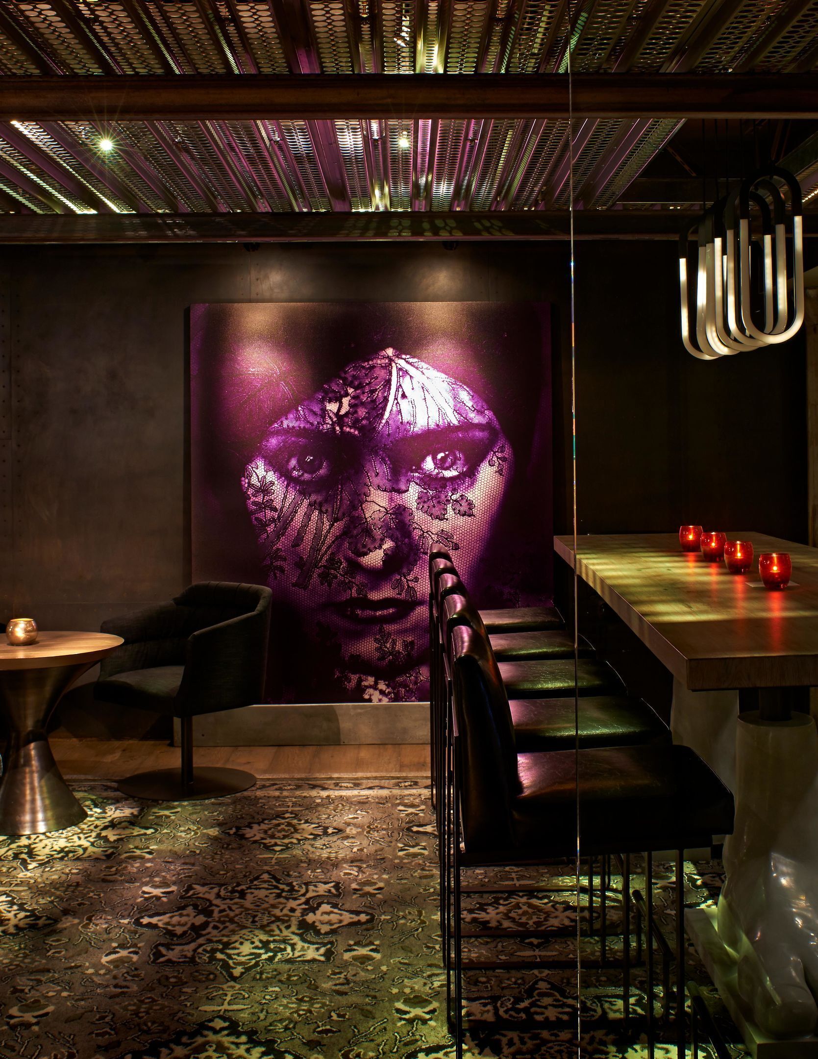 A modern interior with a large wall mural, a dining area with a wooden table and chairs, and a patterned carpet.