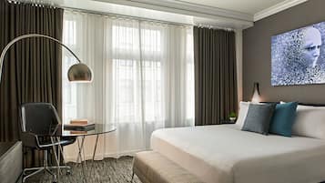 Habitación de hotel con una cama grande, un escritorio con silla, una lámpara y un cuadro en la pared.