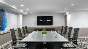 A conference room with a long table, black chairs, a projector screen, and a decorative plant.