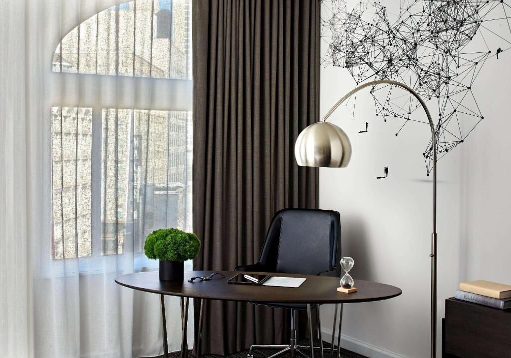 Un espace de bureau moderne comprenant une table ronde, un fauteuil de bureau noir, un lampadaire et un élément décoratif mural.