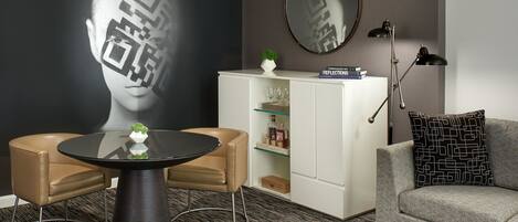 A modern living room with a round table, two chairs, a sofa, a cabinet, and a large mirror on the wall.