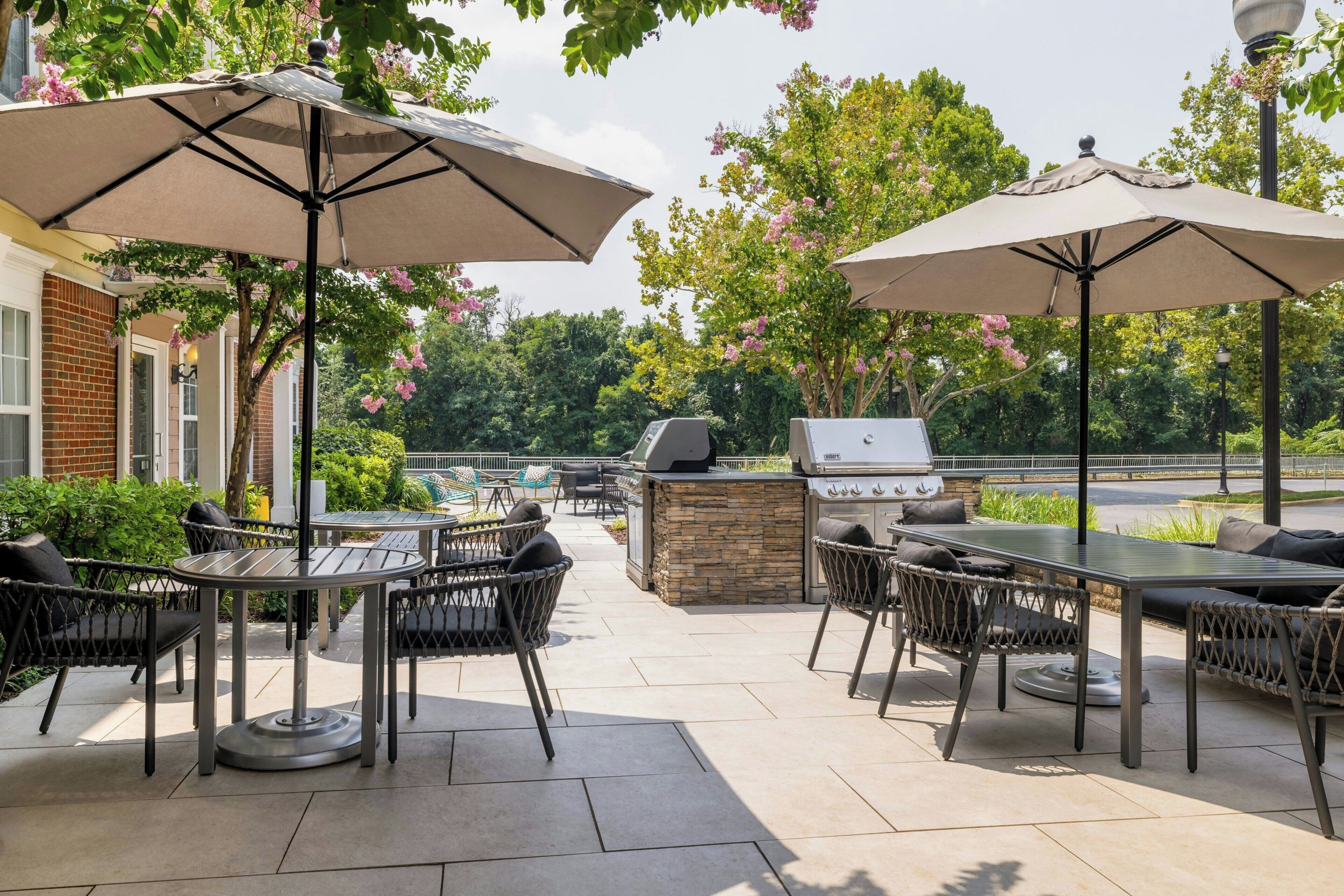 An outdoor patio with a grill, tables, chairs, and umbrellas.
