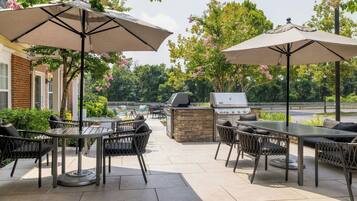 An outdoor patio with a grill, tables, chairs, and umbrellas.