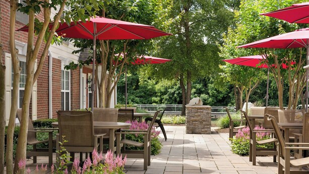 An outdoor patio with brick walls, red umbrellas, and wicker furniture. - TownePlace Suites by Marriott Gaithersburg (Gaithersburg)