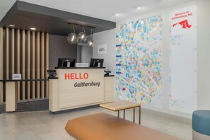 A hotel reception area with a wooden desk, a 'HELLO' sign, a computer, and a colorful map on the wall. - TownePlace Suites by Marriott Gaithersburg (Gaithersburg)