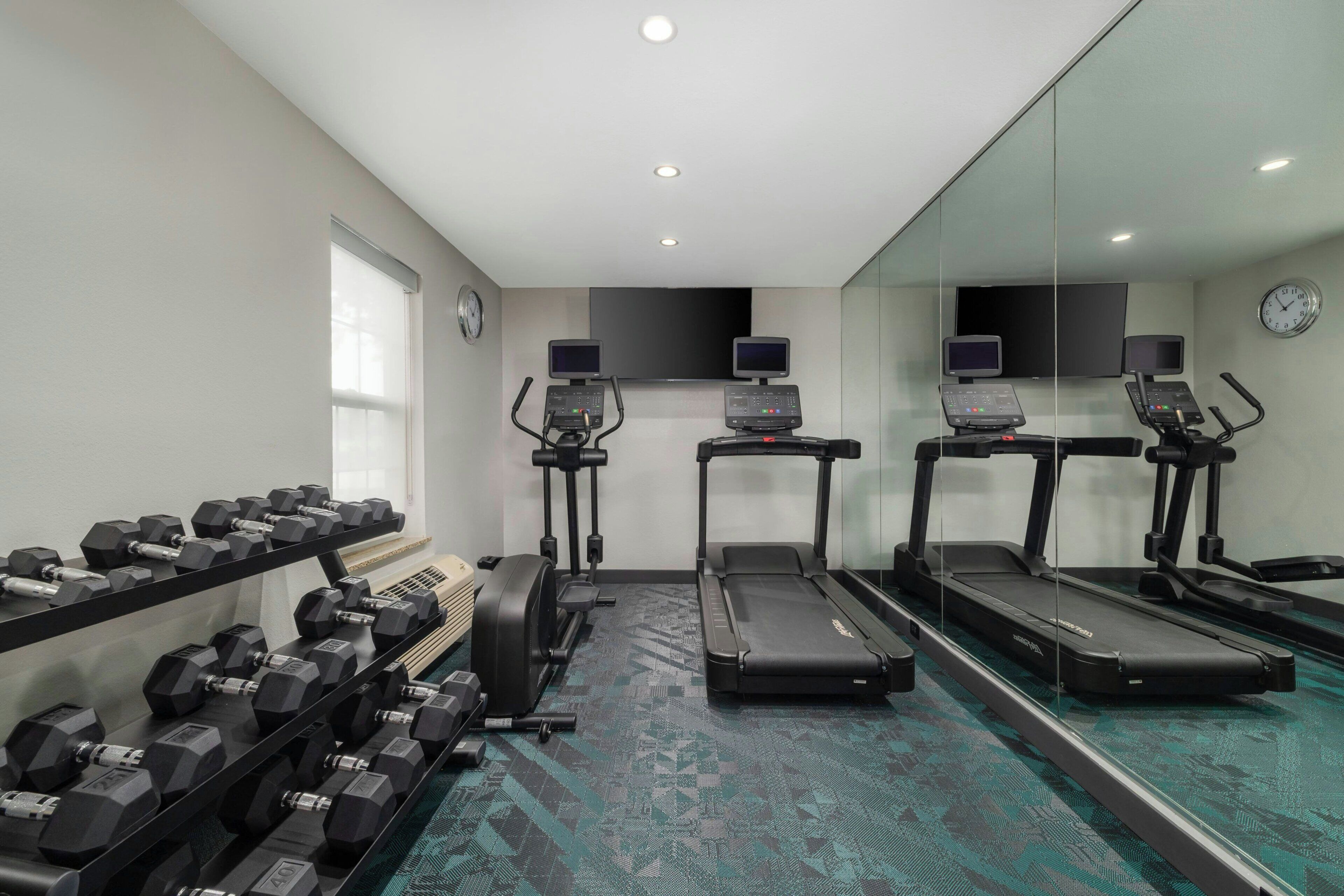 A gym with treadmills, a stationary bike, and a set of dumbbells.