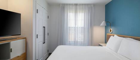 A hotel room with a bed, a TV, a wardrobe, a window with curtains, and a lamp.