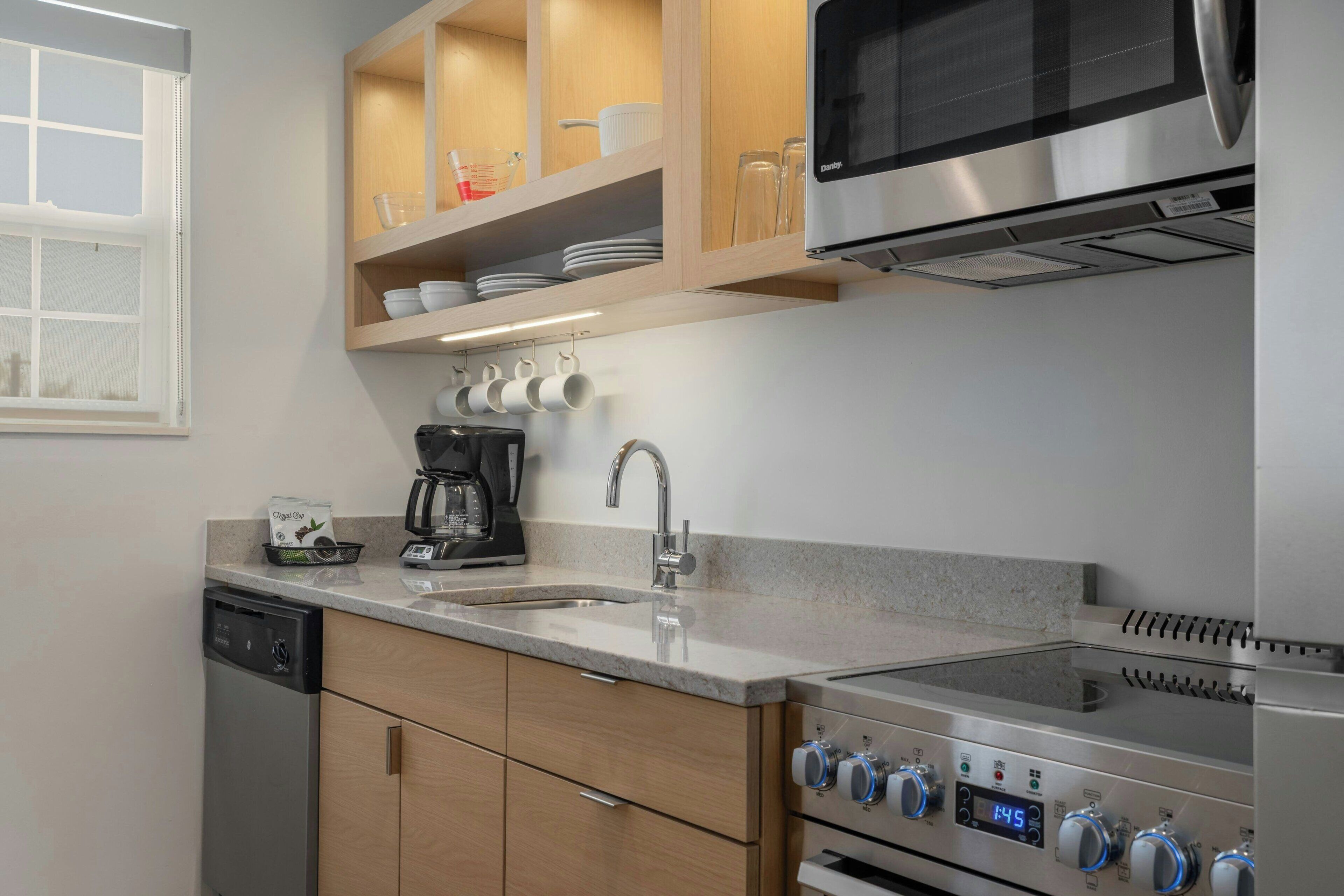 A modern kitchen with a dishwasher, coffee maker, microwave, oven, and a stainless steel range hood.