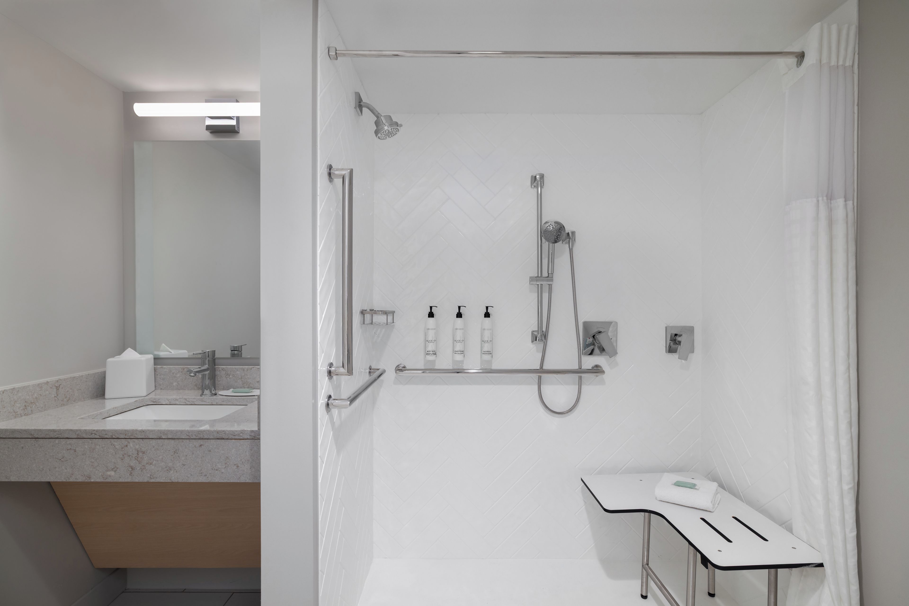 Un baño moderno con ducha, tocador con espejo y artículos de aseo.