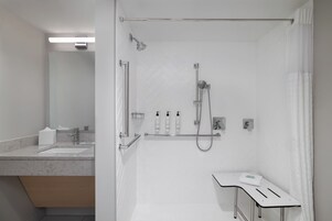 Un baño moderno con ducha, tocador con espejo y artículos de aseo.