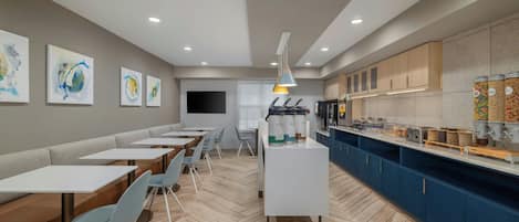 A modern cafe with seating, a counter with food and drink dispensers, and artwork on the walls.