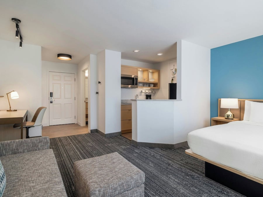 Una habitación de hotel con cama, escritorio, silla, kitchenette y baño.