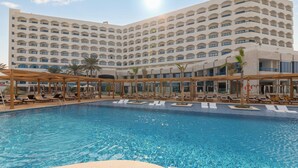 A hotel with a large pool area, multiple lounge chairs, and a multi-story building with balconies. - Dusit Ajman Resort & Villas (Ajman)