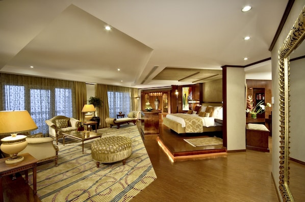 A spacious hotel room with a large bed, a sitting area with a sofa and armchairs, a coffee table, and a dining table. - Dusit Ajman Resort & Villas (Ajman)