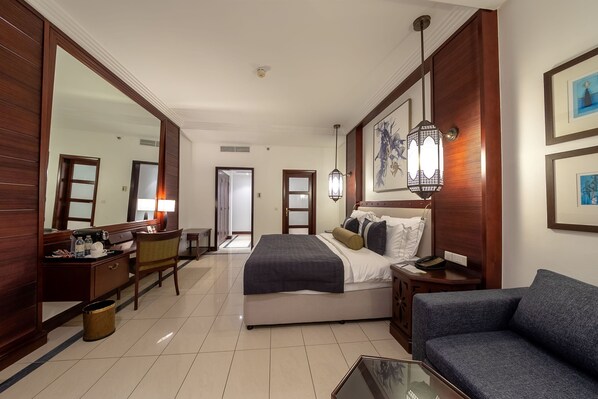 Habitación de hotel con cama, escritorio, silla, sofá, cesto de basura y un espejo grande.