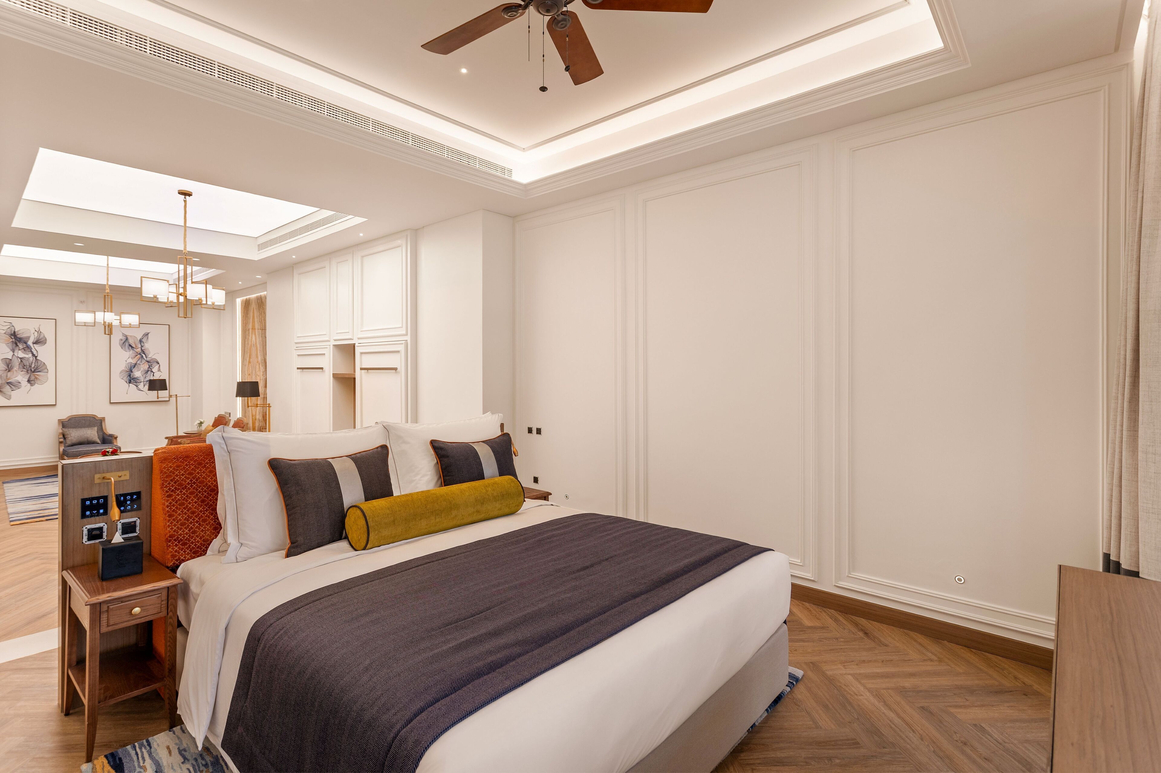 Une chambre d’hôtel moderne dotée d’un grand lit, d’un ventilateur de plafond, d’un bureau avec une lampe et d’œuvres d’art accrochées aux murs.