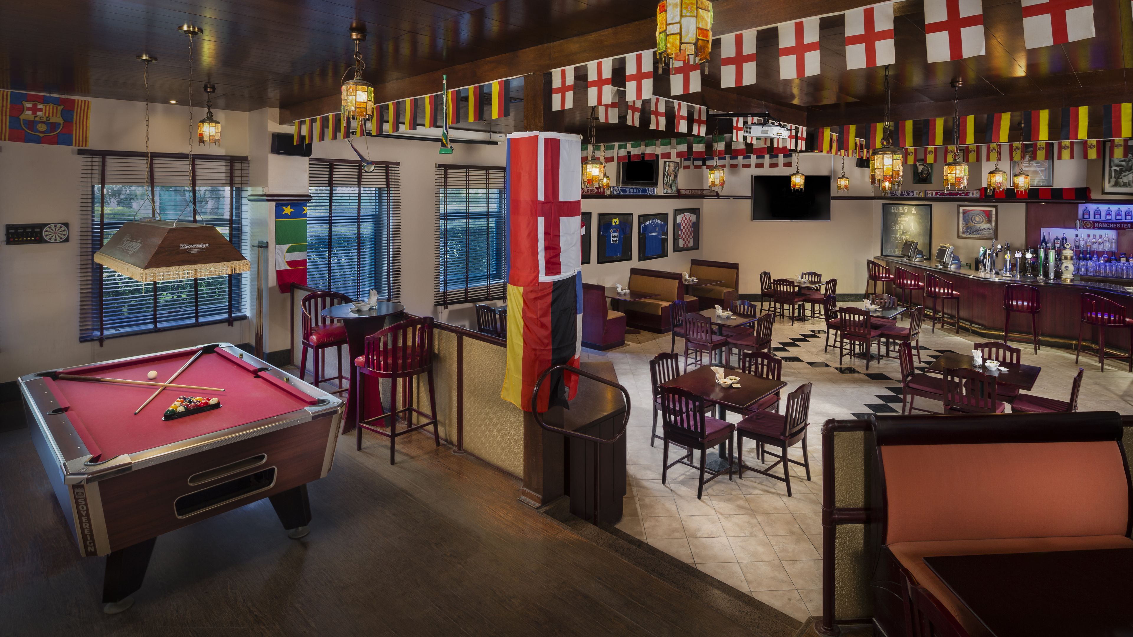 A billiards room with a pool table, multiple seating areas, and a bar with flags.