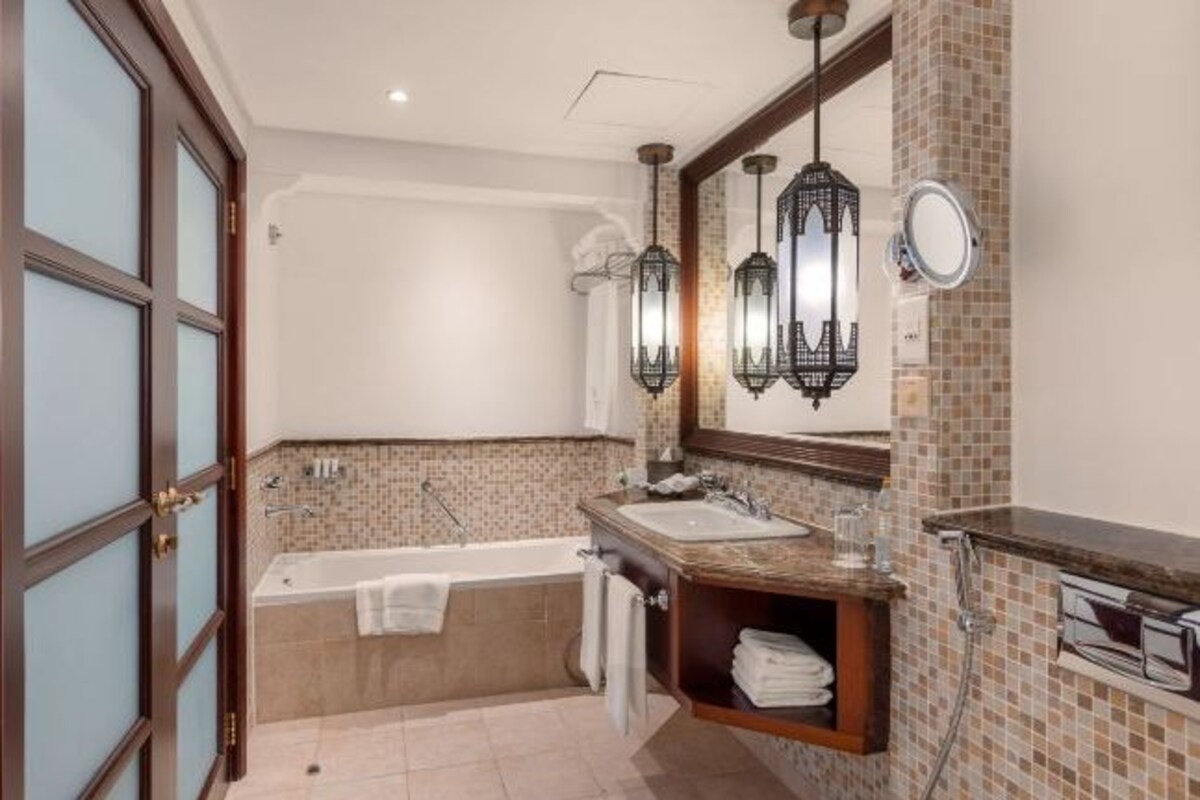 A bathroom with a bathtub, a sink, a mirror, and hanging lanterns.