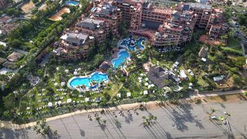 An aerial view of a resort with multiple swimming pools, a beach, and lush landscaping.
