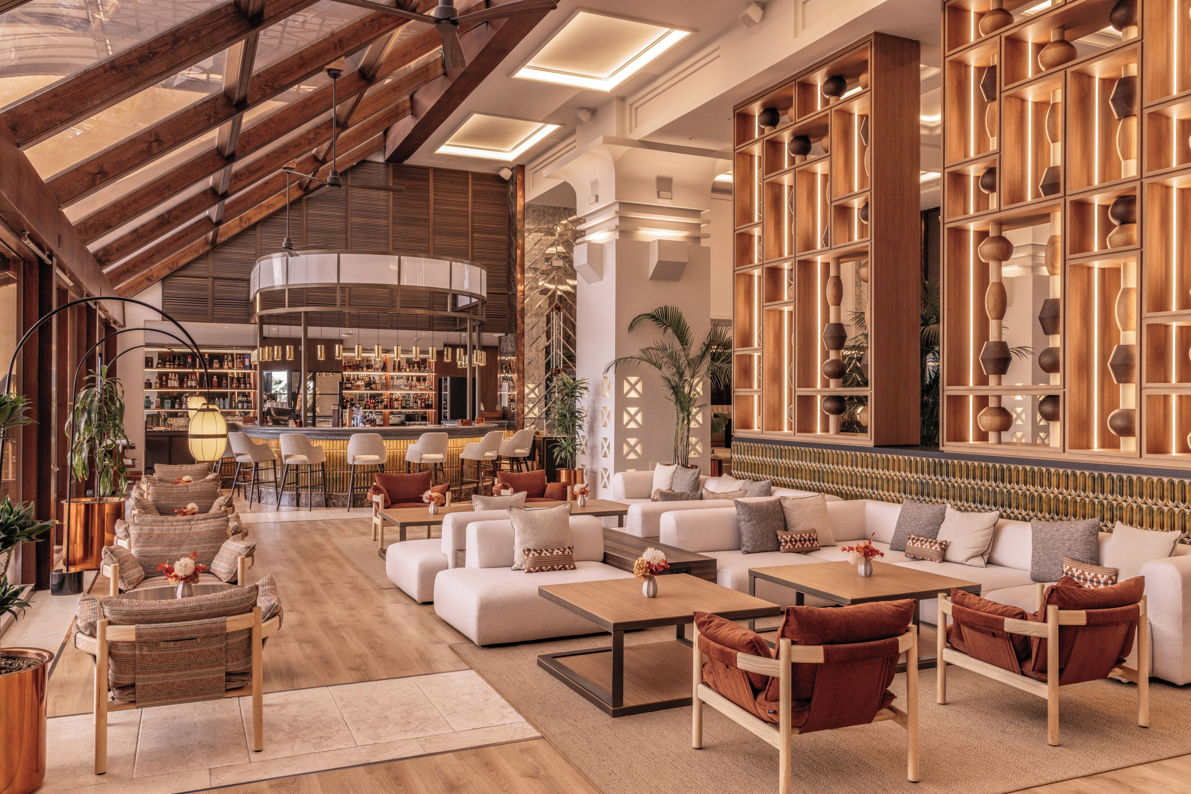 A spacious lounge area with a high ceiling, wooden beams, and a bar with a variety of bottles.