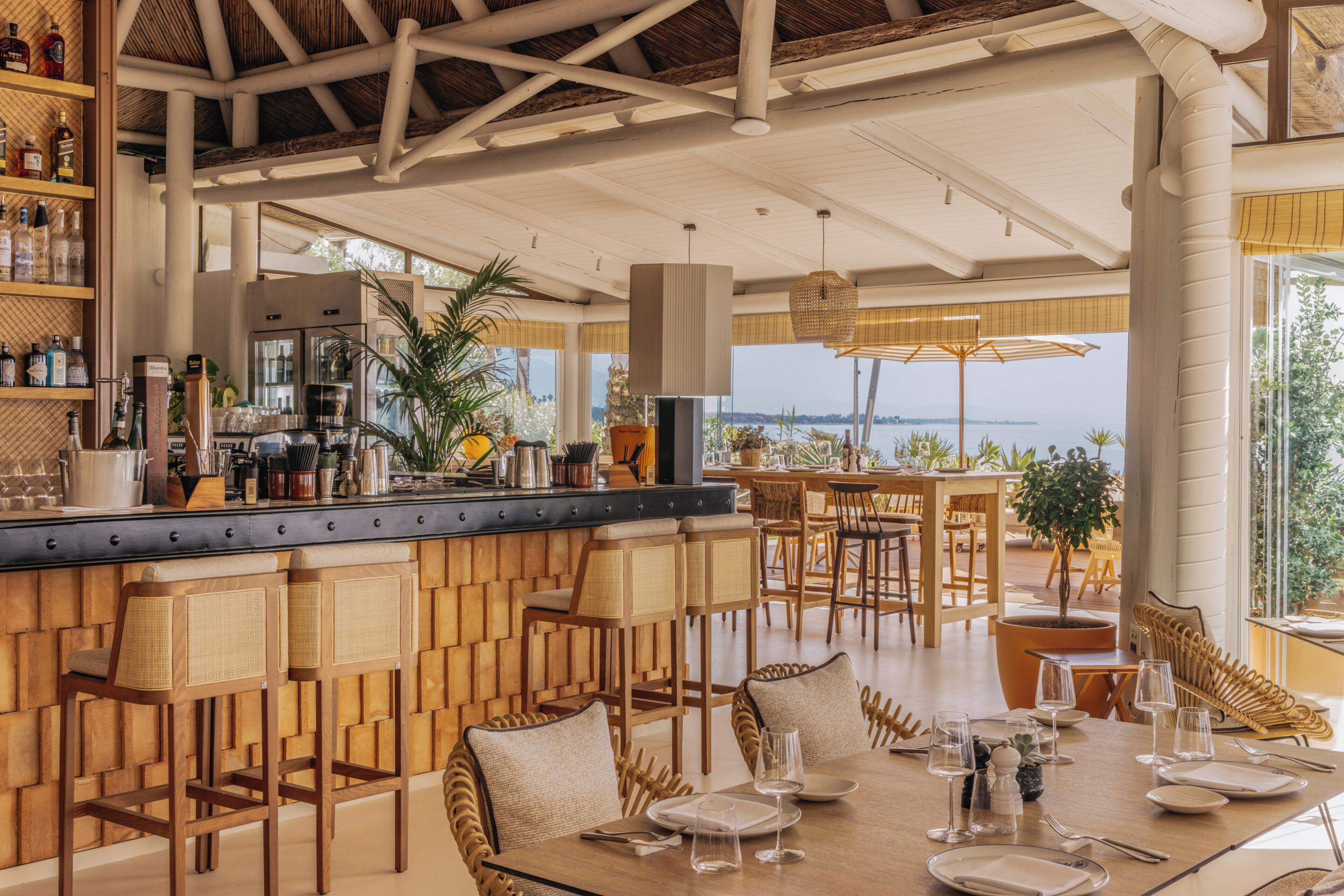 A restaurant with a bar area, wooden furniture, and a view of the sea.
