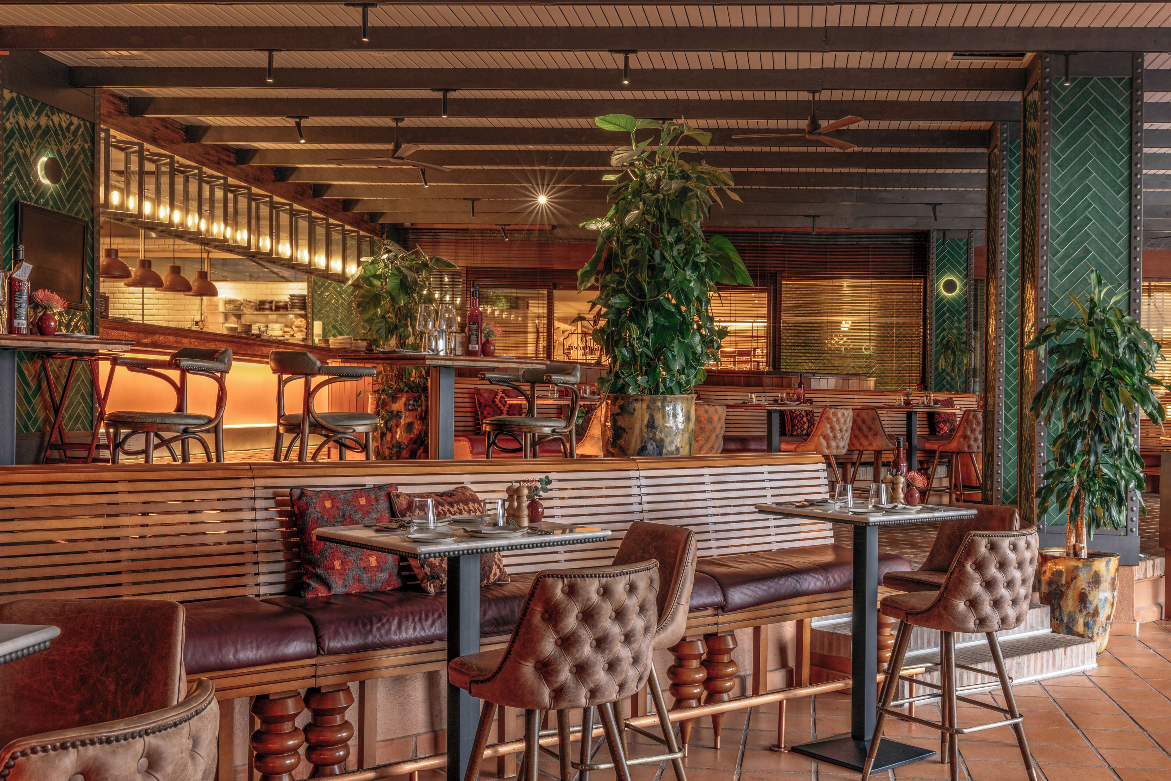 A restaurant interior with a bar area, seating, and decorative plants.