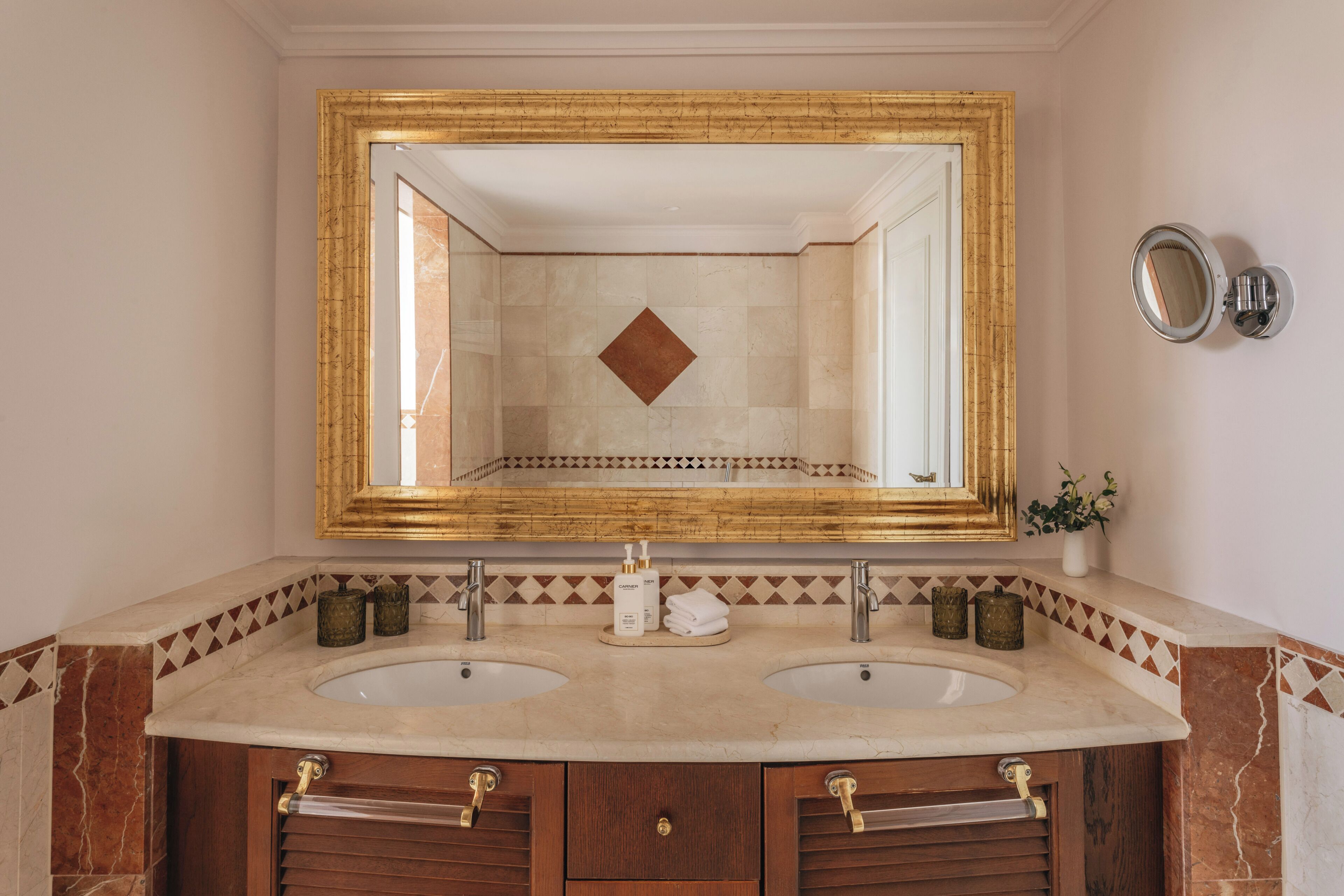 Un baño con dos lavamanos, un espejo grande y un borde decorativo de azulejos.
