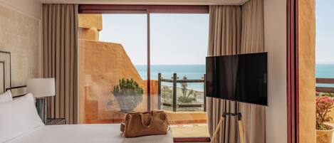 A hotel room with a bed, a TV, a view of the sea, and a balcony.