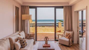 A living room with a sofa, a chair, a coffee table, and a view of the sea through large glass doors.