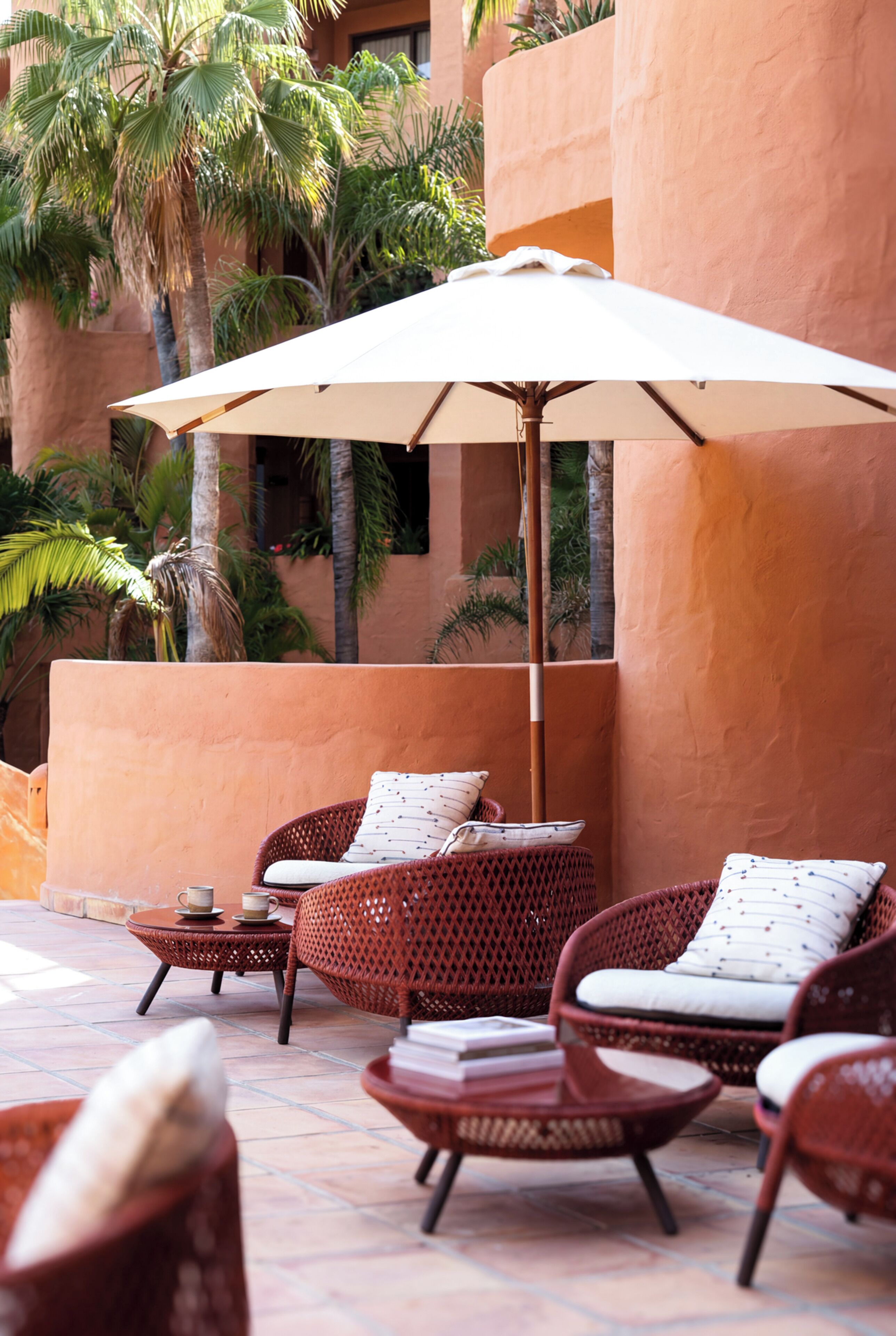 Un espace extérieur aménagé avec des meubles en osier, un grand parasol et des palmiers.