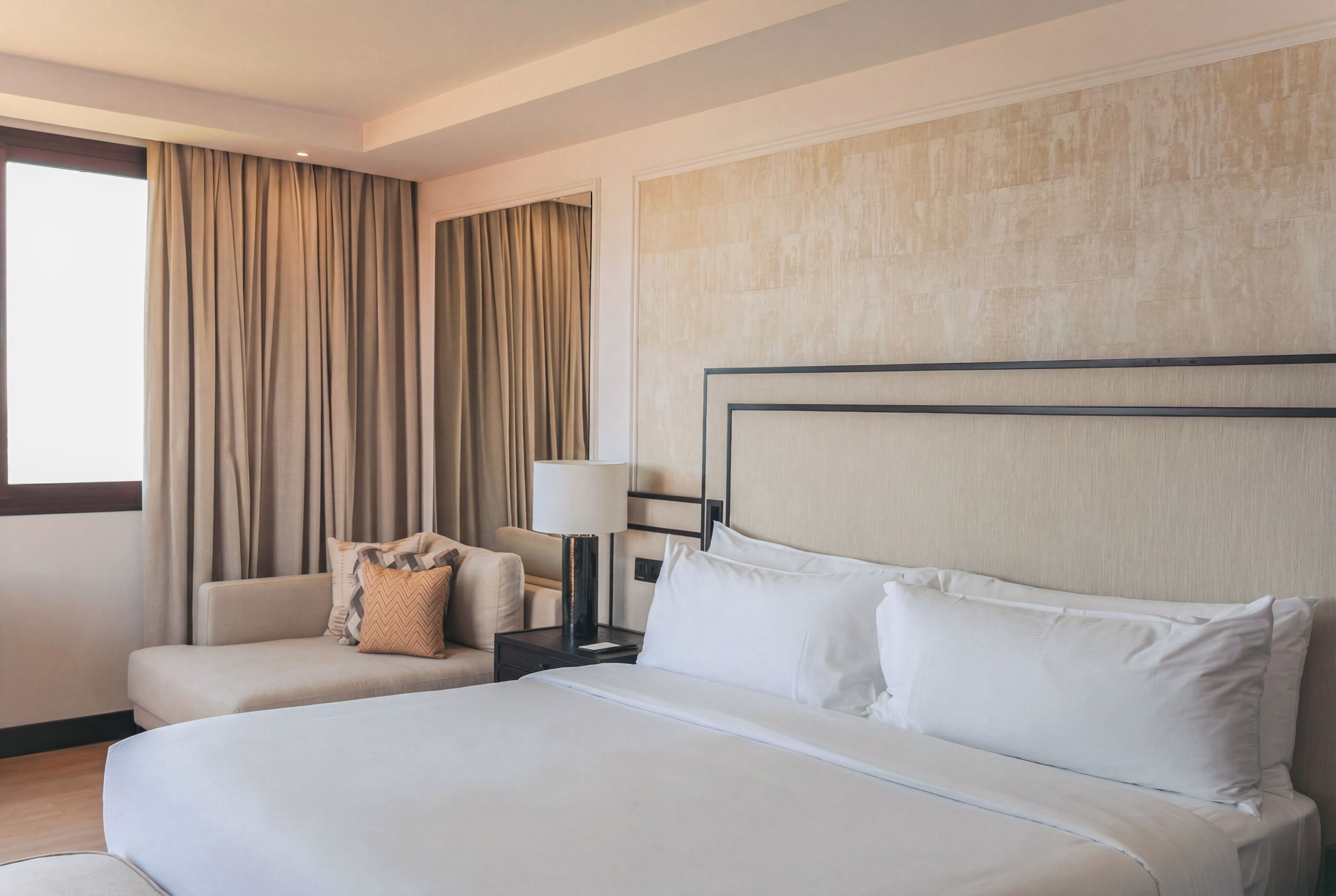 A hotel room with a large bed, a sofa, a nightstand, and a lamp.