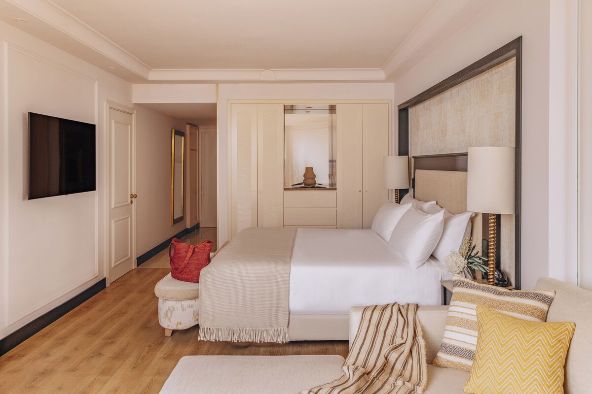 Una habitación de hotel con una cama, un televisor, un sofá y una mesita con una lámpara.